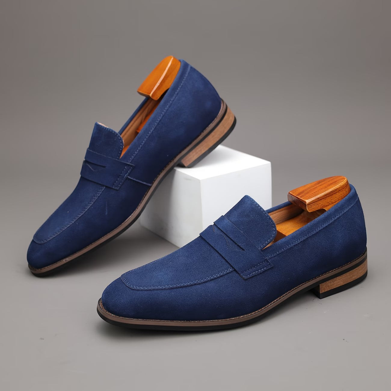 Pair of blue loafers with brown soles on a gray background