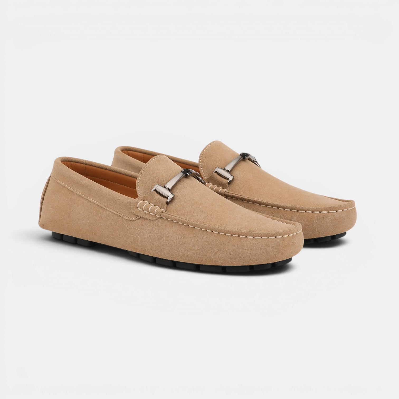 Pair of beige loafers with metallic buckles on a light gray background