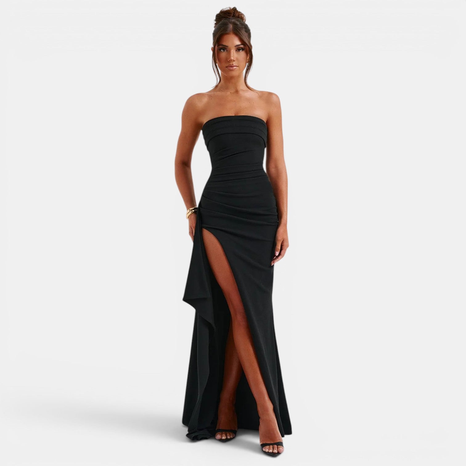 Woman wearing a black strapless gown with a high slit on a white background