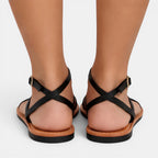 Black strappy sandals on feet with a plain background
