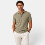 Man wearing a green patterned polo shirt and white pants on a light gray background