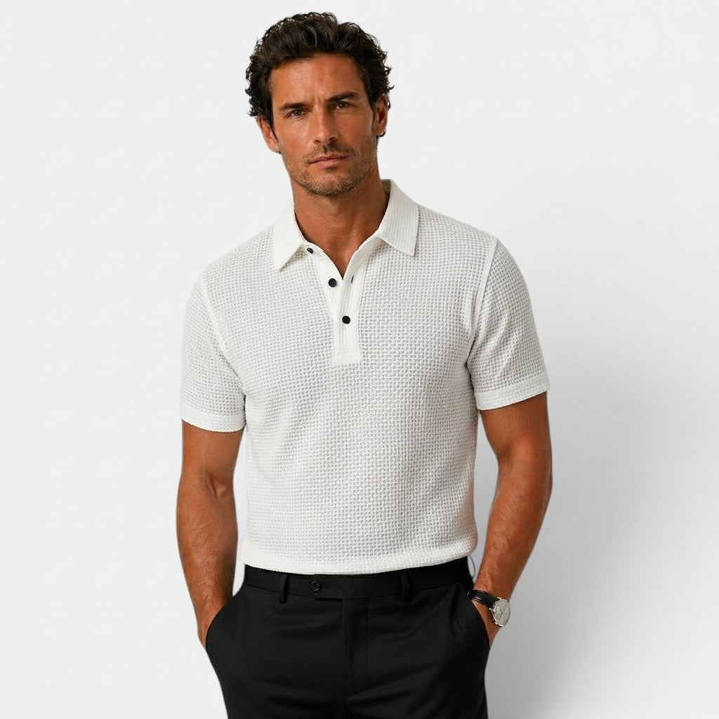 Man wearing a white patterned polo shirt and black pants on a light gray background