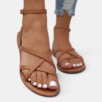 Brown strappy sandals worn with rolled-up jeans on a light gray background