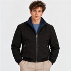Men's black zip-up bomber jacket styled with a blue shirt and beige trousers