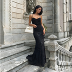 Woman in a black evening gown standing on stone steps with a white handbag.