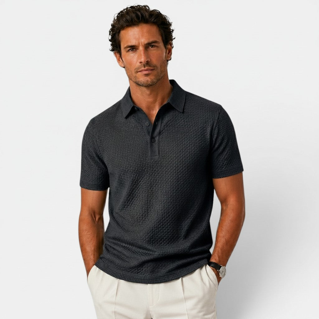 Man wearing a dark patterned polo shirt and light pants on a plain background
