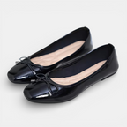 Pair of black patent leather shoes with bow details on a light gray background