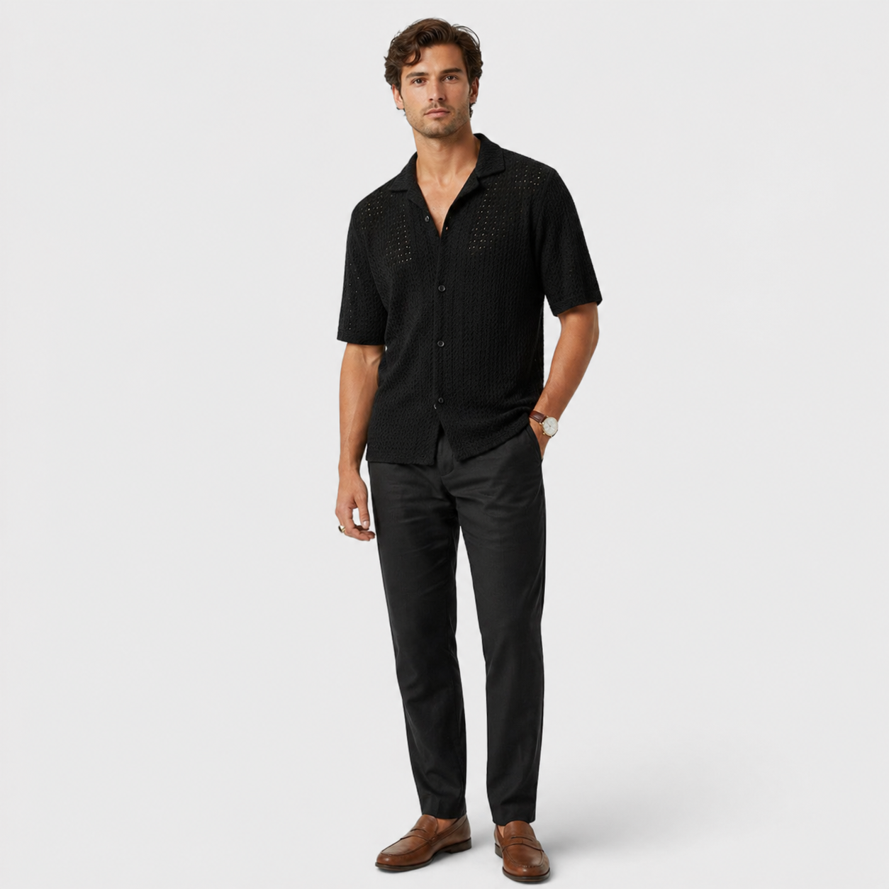Man wearing a black patterned shirt and black pants on a white background