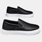 Two black slip-on shoes with white soles on a light gray background