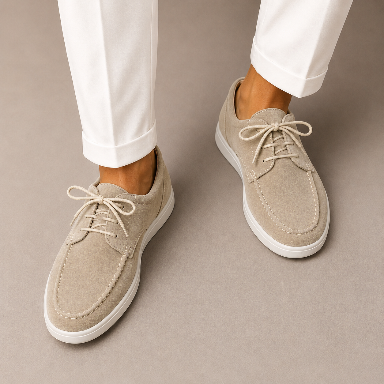 Beige suede shoes with white laces worn with white pants on a beige background