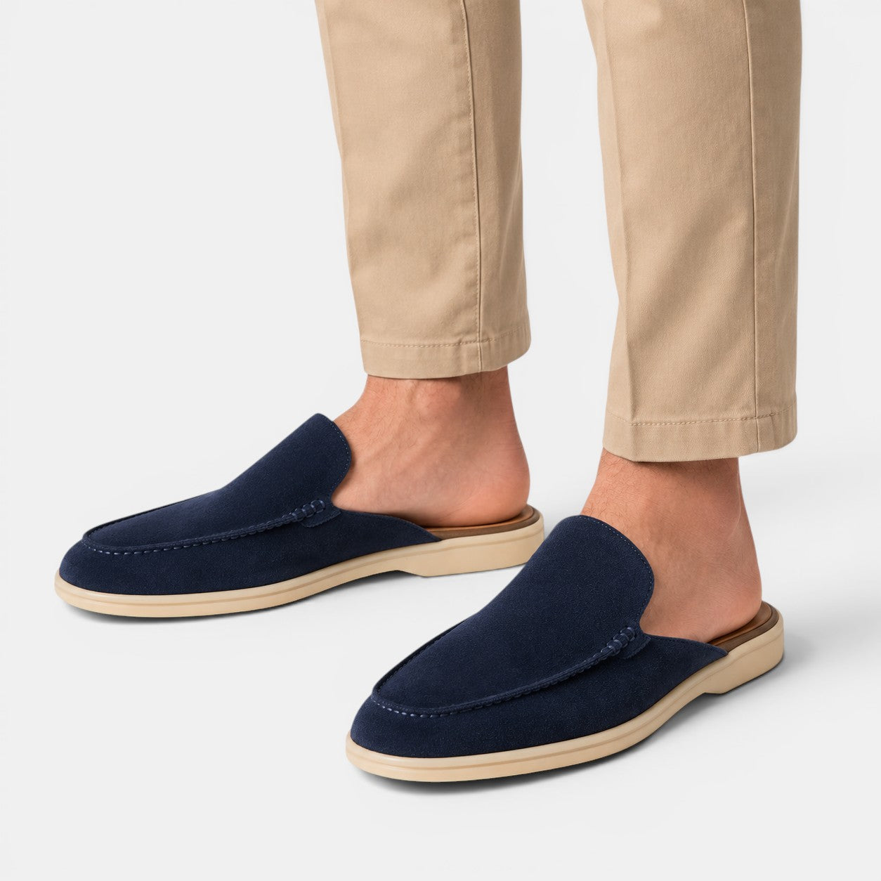 Navy loafers worn with beige pants on a light gray background