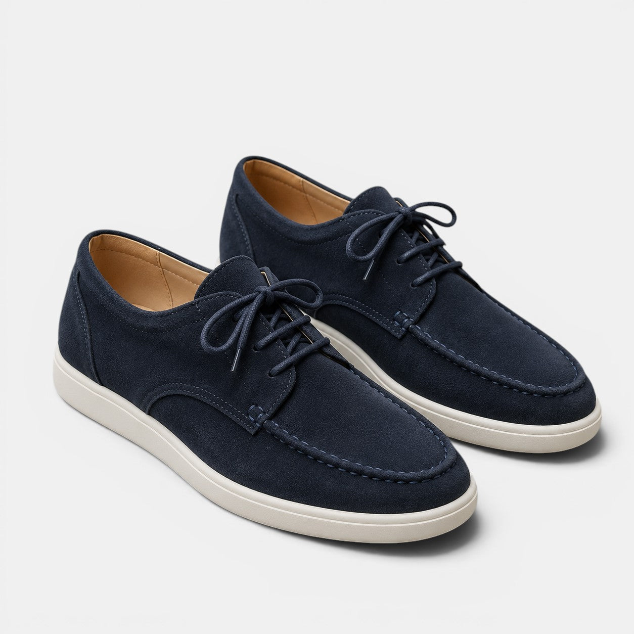 Pair of navy blue suede shoes with white soles on a light gray background