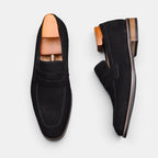 Pair of black suede loafers with wooden soles on a light gray background