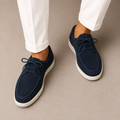 Navy blue loafers with white soles worn with white pants on a beige background