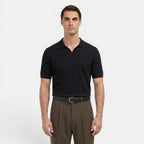 Man wearing a black polo shirt and brown pants on a white background