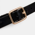 Black belt with a gold buckle on a light gray background
