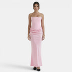 Woman wearing a strapless blush pink maxi dress with a fitted corset bodice and draped waist detail.