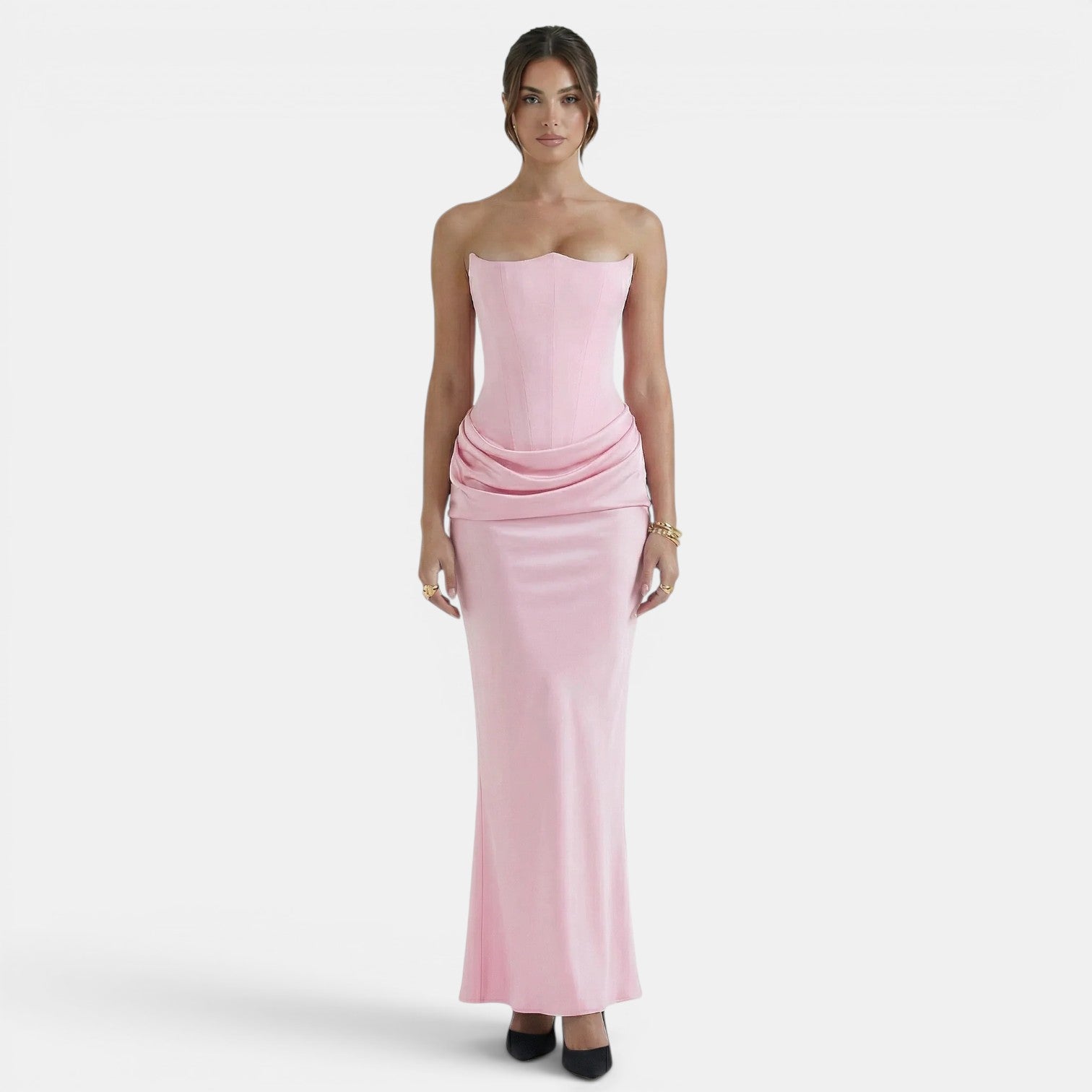 Woman wearing a strapless blush pink maxi dress with a fitted corset bodice and draped waist detail.