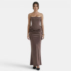 Woman wearing a strapless mocha maxi dress with a fitted corset bodice and draped waist detail.
