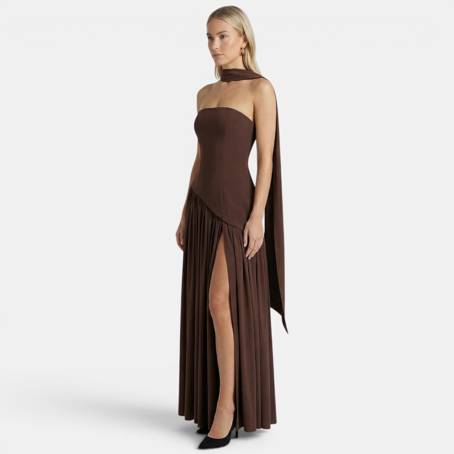 Side view of a woman wearing a dark brown strapless maxi dress with a scarf neckline and thigh-high slit against a light gray background.