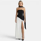 Woman wearing a black-and-white strapless maxi dress with a scarf neckline and thigh-high slit, standing against a light gray background.