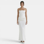 Woman wearing a strapless white maxi dress with a fitted corset bodice and draped waist detail.