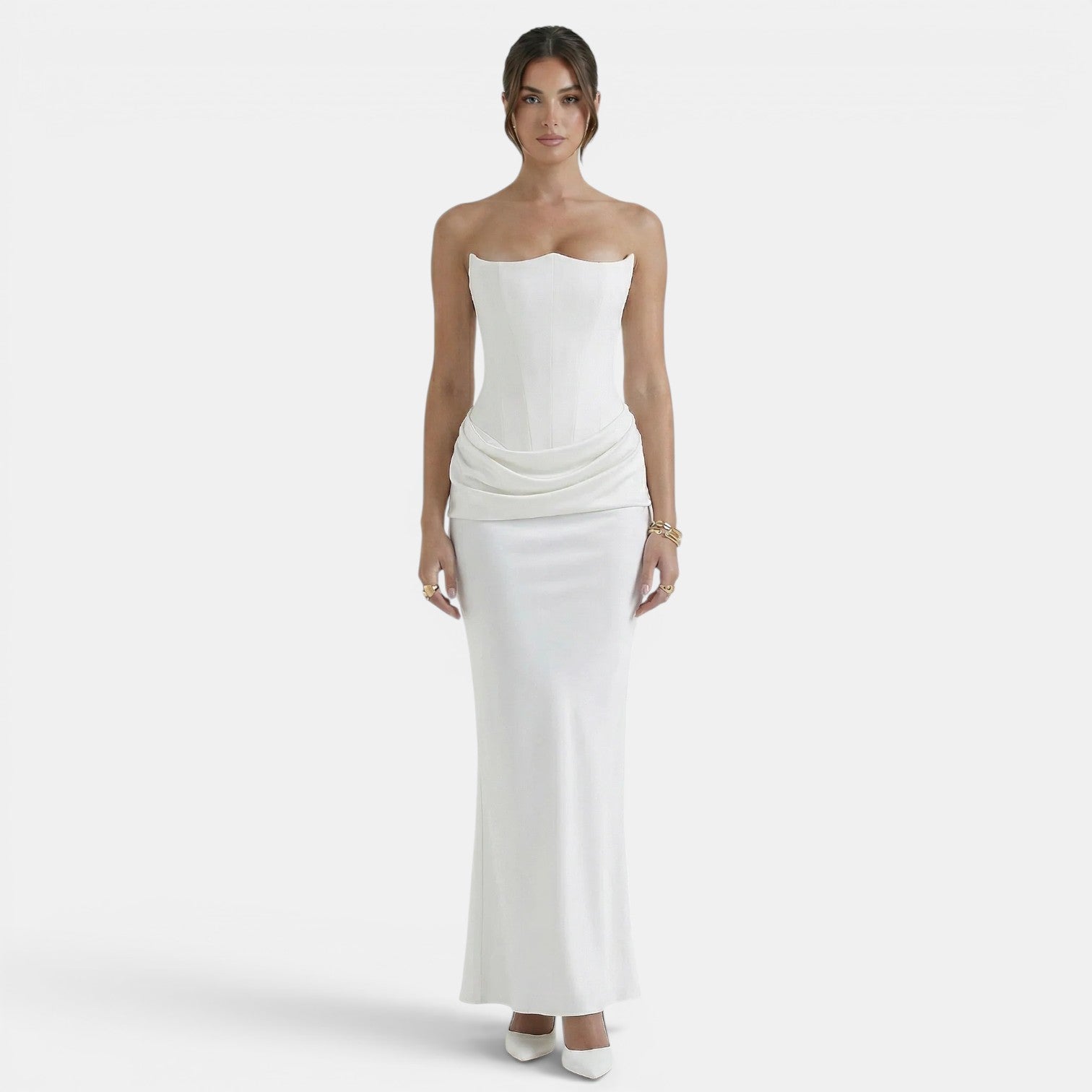 Woman wearing a strapless white maxi dress with a fitted corset bodice and draped waist detail.