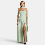Woman wearing a sage green strapless maxi dress with a scarf neckline and thigh-high slit, standing against a light gray background.