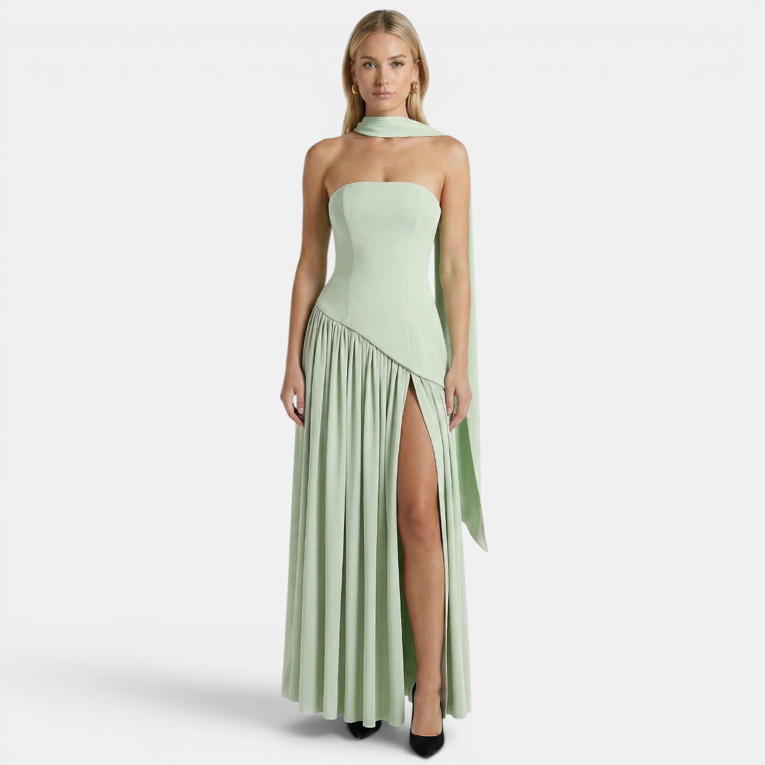 Woman wearing a sage green strapless maxi dress with a scarf neckline and thigh-high slit, standing against a light gray background.