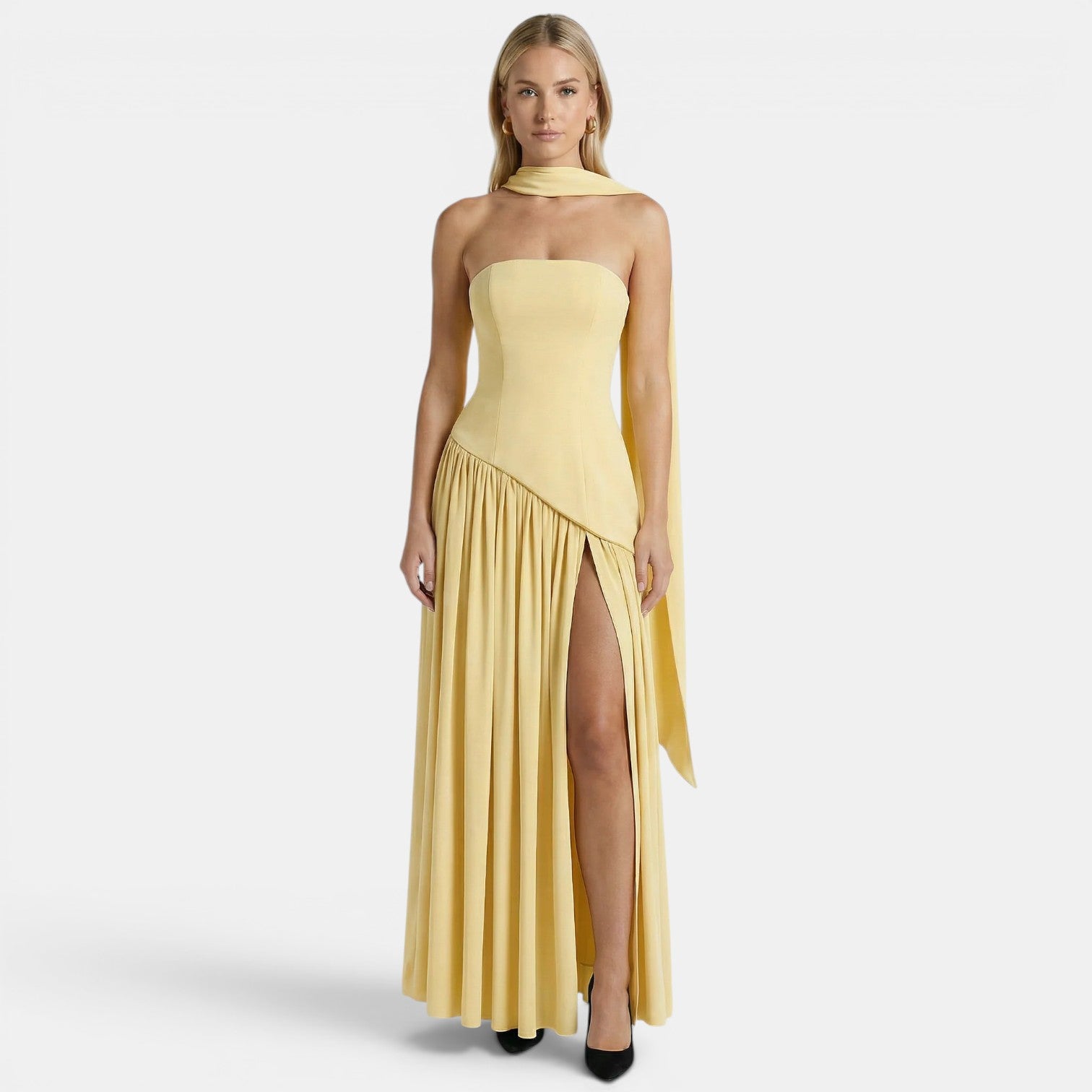 Woman wearing a pale yellow strapless maxi dress with a scarf neckline and thigh-high slit, standing against a light gray background.