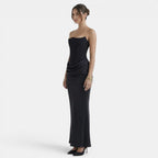 Side view of a woman wearing a strapless navy maxi dress with a fitted bodice and draped skirt.
