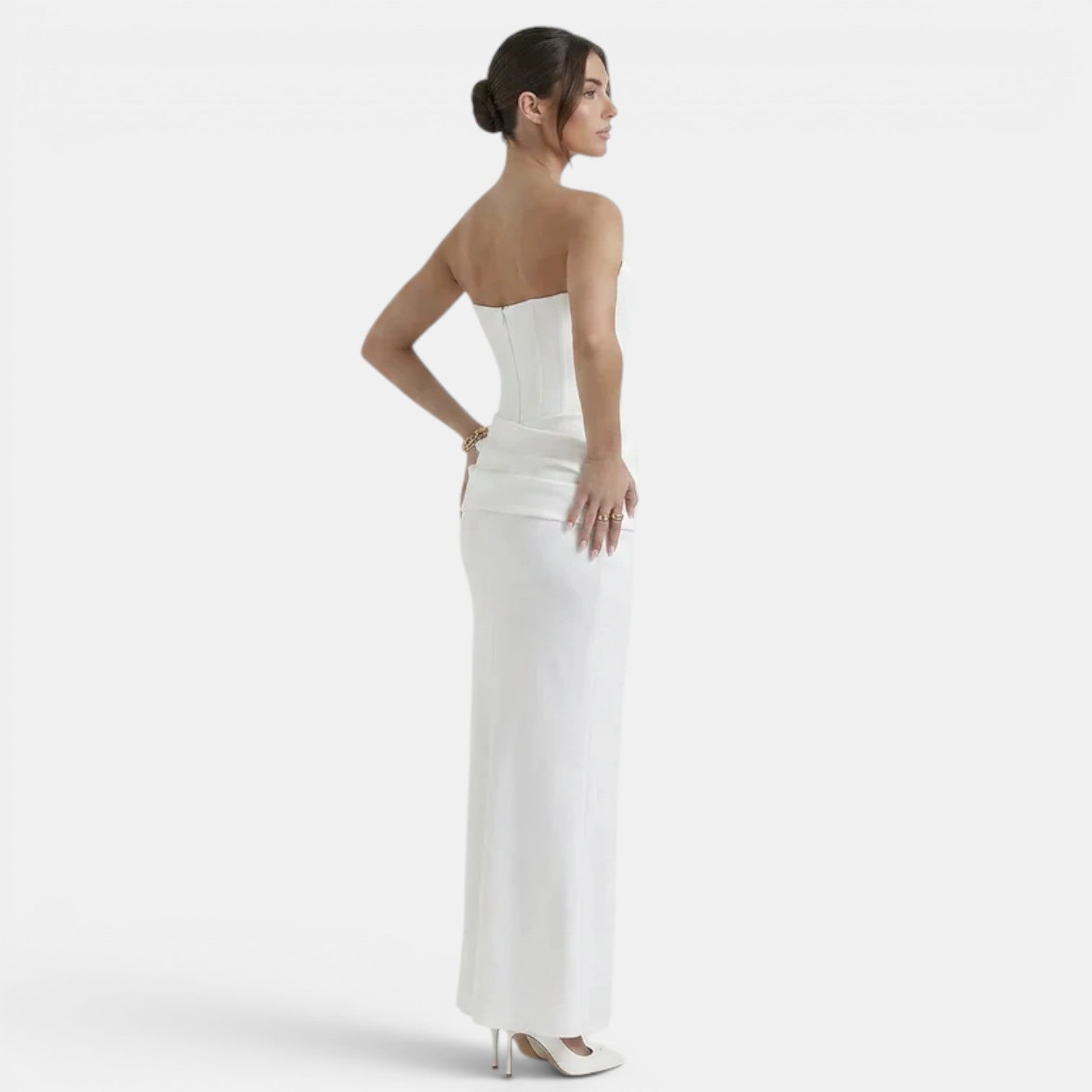 Side back view of a woman wearing a strapless white maxi dress with a fitted corset bodice.