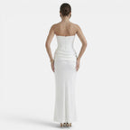 Back view of a woman wearing a strapless white maxi dress with a fitted corset bodice and draped waist detail.