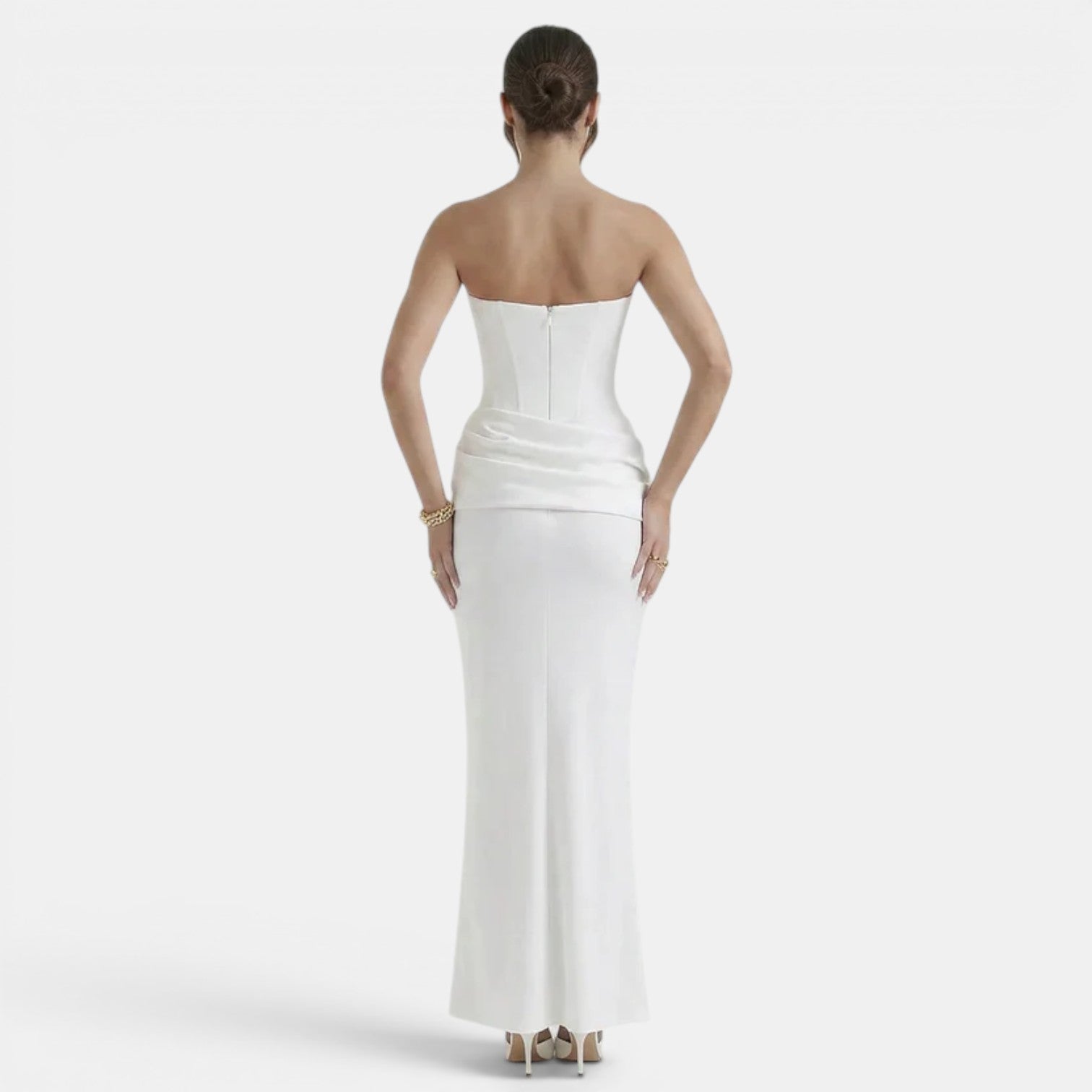Back view of a woman wearing a strapless white maxi dress with a fitted corset bodice and draped waist detail.