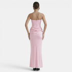 Back view of a woman wearing a strapless blush pink maxi dress with a fitted corset bodice and draped waist detail.
