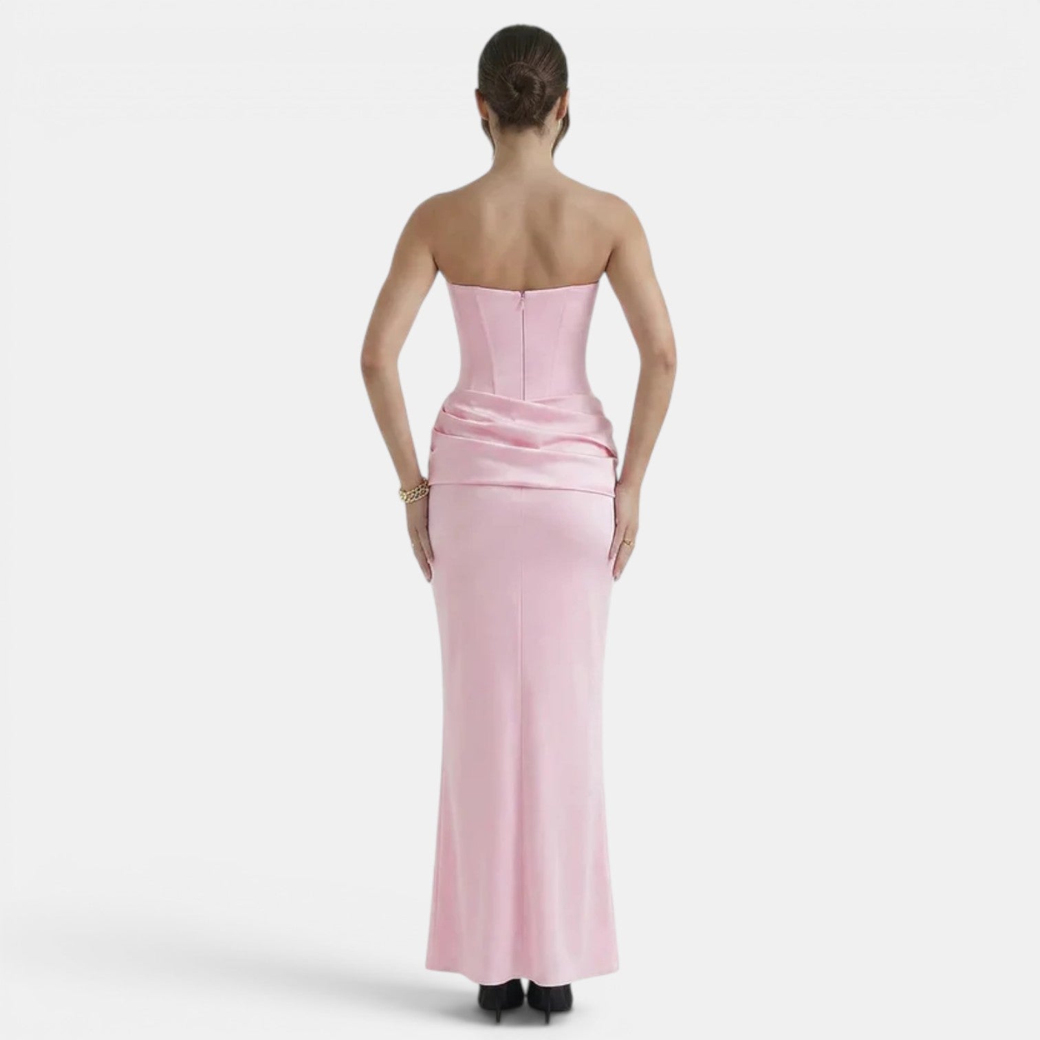 Back view of a woman wearing a strapless blush pink maxi dress with a fitted corset bodice and draped waist detail.