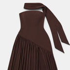 Dark brown strapless maxi dress with a matching scarf detail, pleated skirt, and thigh-high slit, displayed against a light gray background.