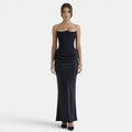 Woman wearing a strapless navy maxi dress with a fitted bodice and draped skirt.