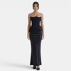 Woman wearing a strapless navy maxi dress with a fitted bodice and draped skirt.