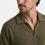Close-up of an olive green textured knit polo shirt with an open collar, highlighting the fabric pattern and neckline.