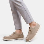 Person wearing beige suede lace-up shoes with white soles and light gray trousers, shown in a side walking pose.