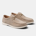 Pair of beige suede lace-up shoes with white soles, displayed against a light gray background.