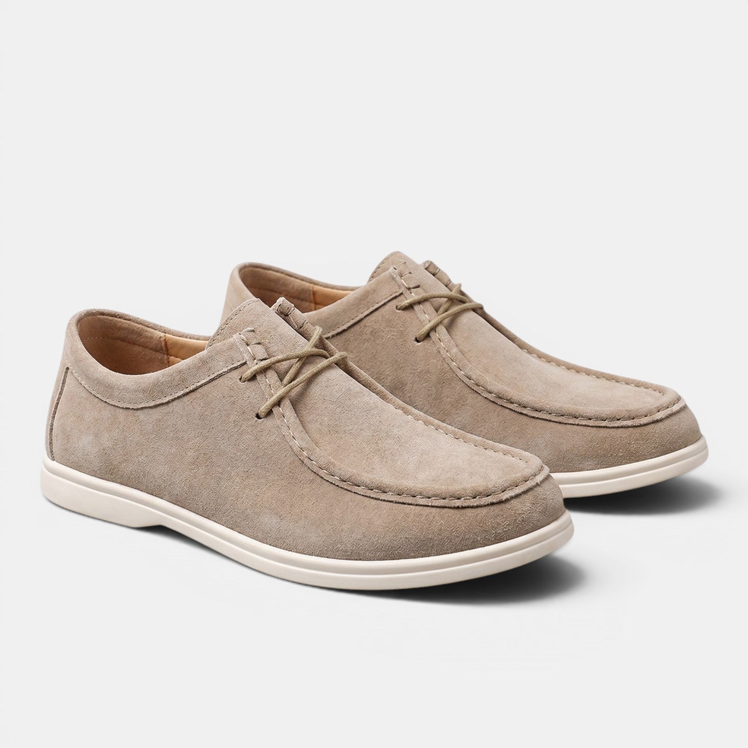 Pair of beige suede lace-up shoes with white soles, displayed against a light gray background.