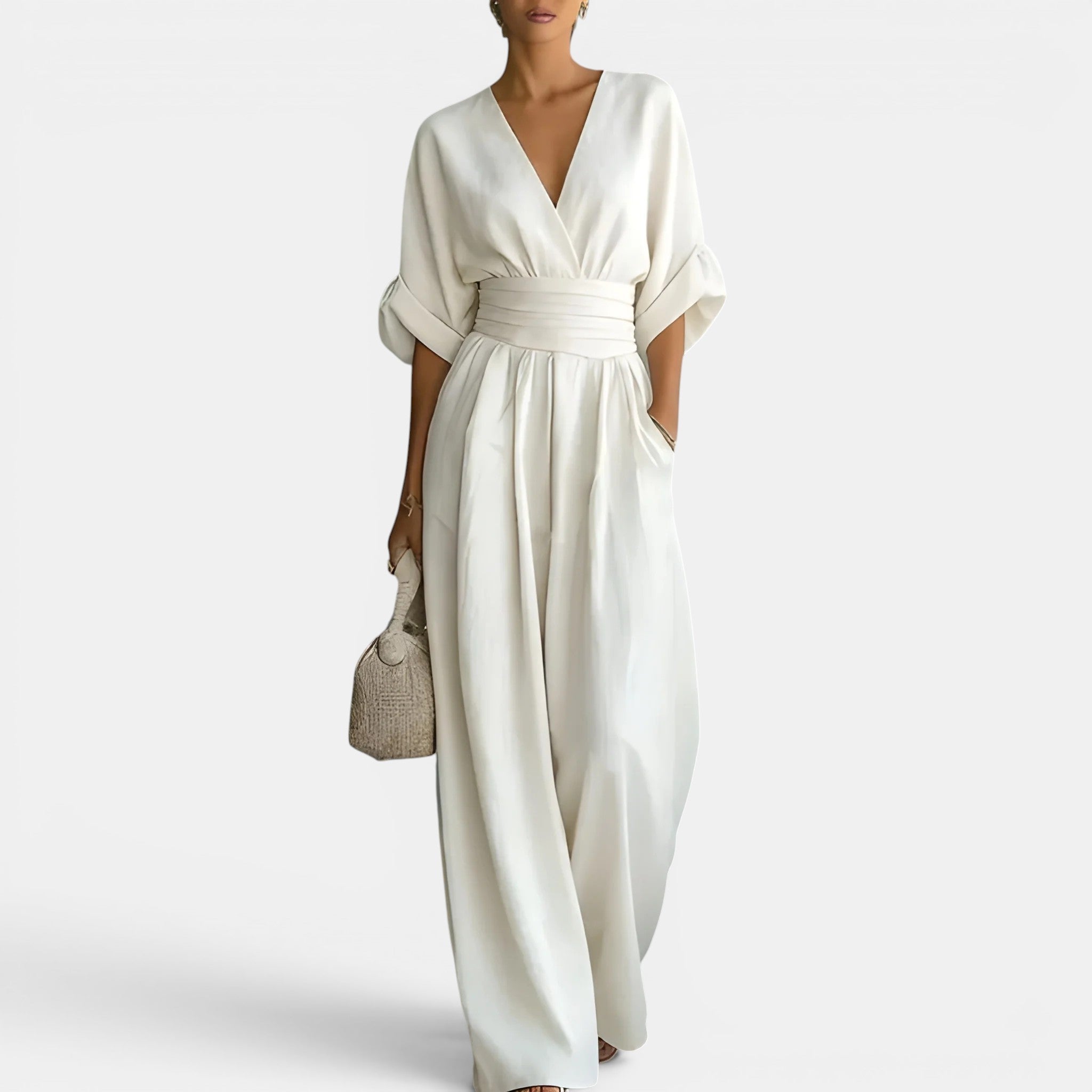 Woman wearing a white jumpsuit holding a woven bag on a white background