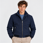 Men's black zip-up bomber jacket styled with a blue shirt and beige trousers