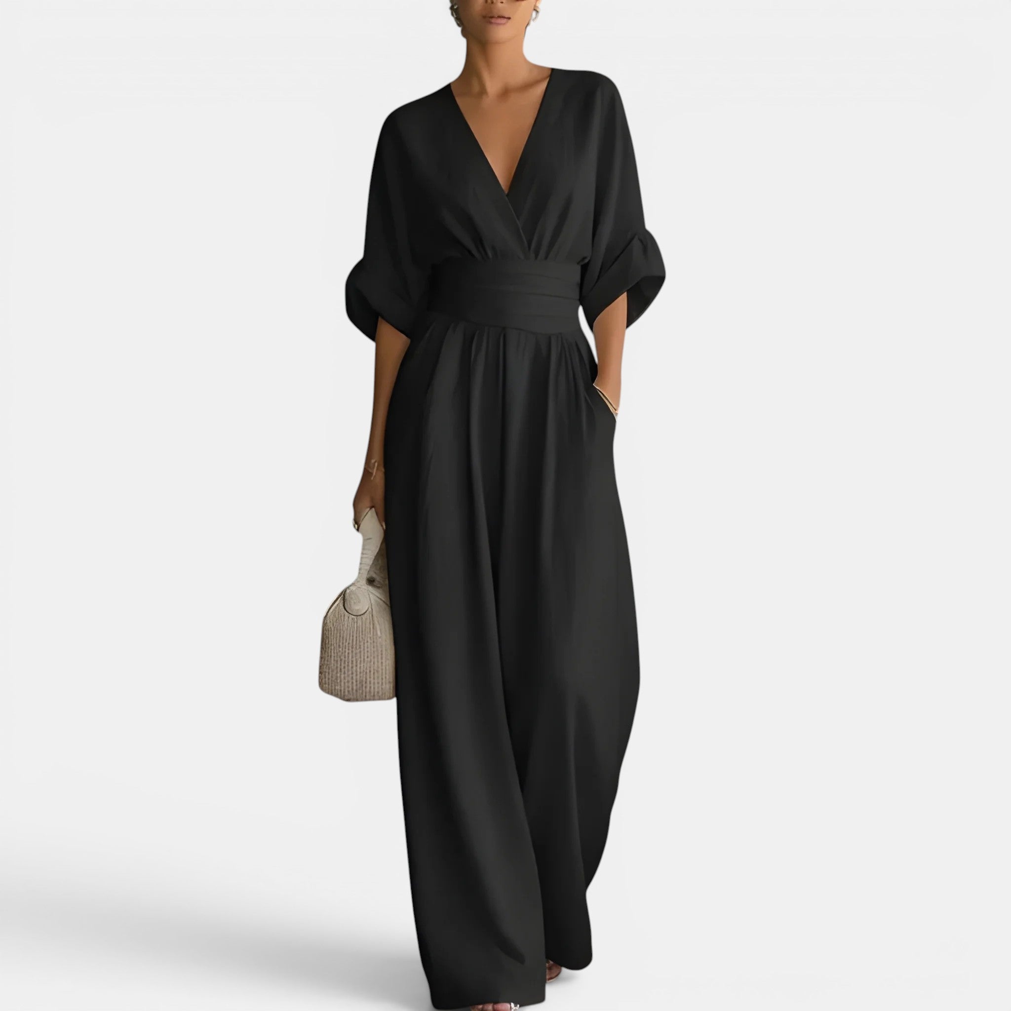 Woman wearing a black jumpsuit holding a beige handbag on a white background