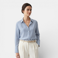Woman wearing a blue striped shirt and white pants on a light gray background