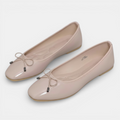 Pair of beige patent leather shoes with bow details on a white background