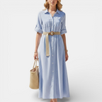 Woman wearing a light blue striped dress with a beige belt on a white background