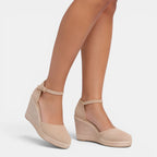 Beige wedge sandals worn by a person on a white background